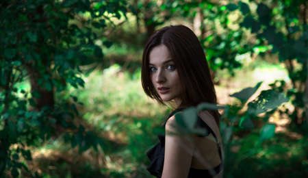 Beautiful brunette girl with blue eyes in the forest. Witching look. Sun spots and glare. Effective bokeh. Selective focus. Blurred background.の写真素材