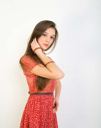 Portrait of a girl with loose dark hair in a red dress on a light background.の写真素材