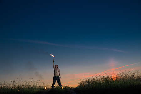 Man stands with signal torches against dark sunset sky