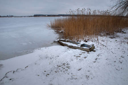 Boat by the river in winter. The boat was frozen into the ice on the shore of the lake among the reeds.の写真素材