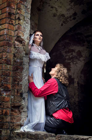 A young man in a red shirt and a beautiful pale witch in an old brick castle. Declaration of love on Halloween.の写真素材