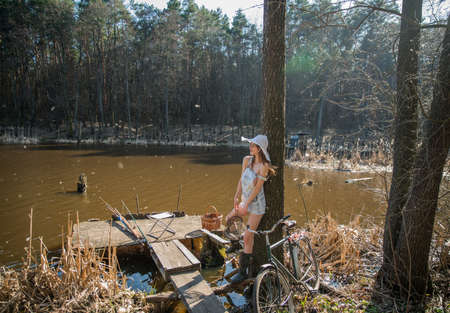 A girl in denim shorts and an old bicycle by the lake on a warm summer day in the evening sunlight.の写真素材