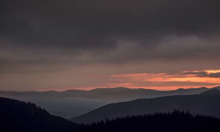 Disturbing sunrise in the mountains. Magnificent view of the clouds illuminated by the rising sun.