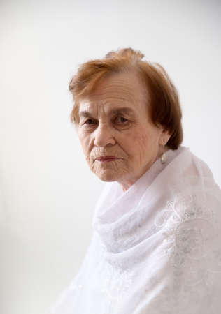Portrait of an elderly wrinkled woman - an old woman in a headscarf on a white background in light clothes.の写真素材
