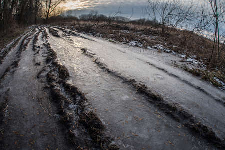 icy country road. A furrow from the wheels of a car. Clouds in the evening sky.の写真素材