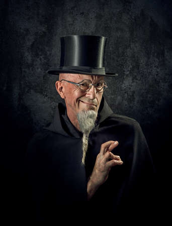 Portrait of a mysterious male magician in a black high top hat and black robe.
