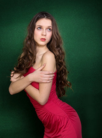 A girl in a red dress with bare shoulders in the studio on a green background.の写真素材
