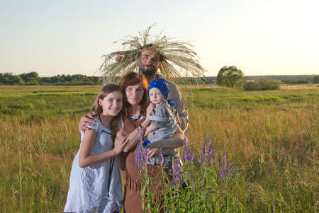 A family with wreaths of flowers and meadow grasses on their heads in the evening lighting on the field.の写真素材