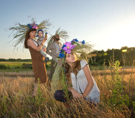 A family with wreaths of flowers and meadow grasses on their heads in the evening lighting on the...