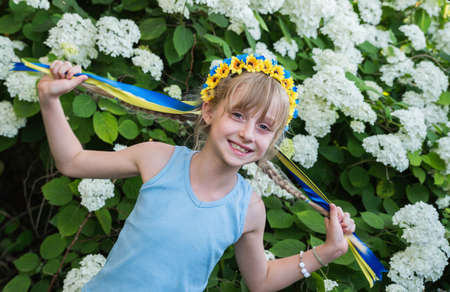 A girl in a blue-yellow Ukrainian wreath with ribbons in the color of the Ukrainian flag against the...