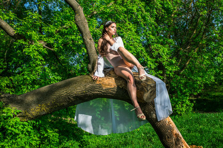 A girl in a bathing suit and a white cape near a broken tree among greenery.の写真素材