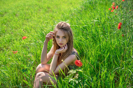 Girl on the background of a green meadow among red poppies.の写真素材