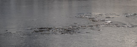 The texture of thin melting ice on a spring lake with the sky reflected on the surface. Light glare.