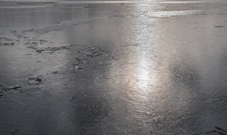 The texture of thin melting ice on a spring lake with the sky reflected on the surface. Light glare.