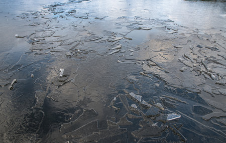 The texture of thin melting ice on a spring lake with the sky reflected on the surface. Light glare.の写真素材