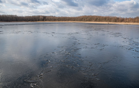 Spring lake covered with thin transparent cracking ice.の写真素材
