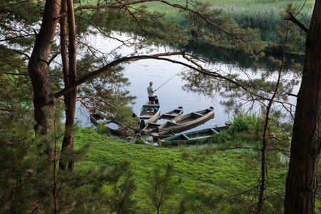 A fisherman is fishing with a fishing rod from a boat in the river. Top view through tree branches.の写真素材