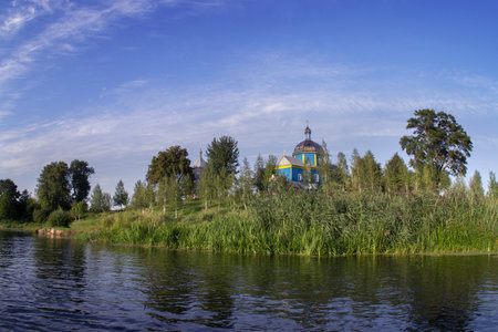 An old wooden beautiful Orthodox church among the trees on the banks of the river against a blue cloudy sky.の写真素材