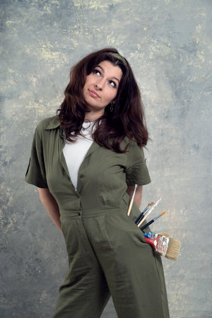 The artist is a woman in a green overalls and with brushes stained in paint on a studio background.の写真素材