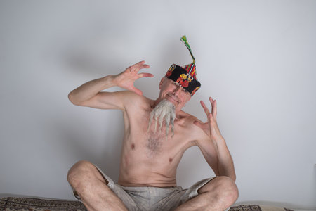 A man with pigtails on a gray beard in a skullcap with a naked torso.の写真素材