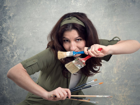 The artist is a woman in a green overalls and with brushes stained in paint on a studio background.の写真素材