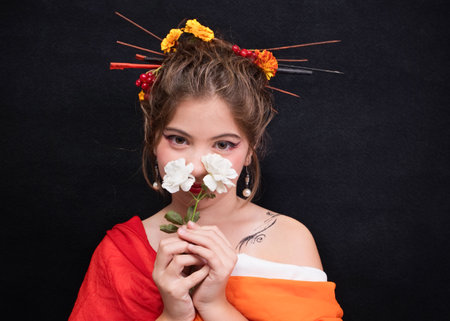 Portrait of a girl in bright traditional Japanese clothes with a white rose on a dark background.の写真素材