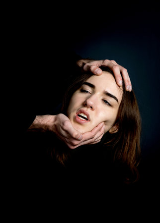 Mens hands hold a womans head on a black background. Fear, suffering.の写真素材