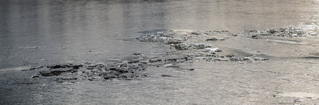 The texture of thin melting ice on a spring lake with the sky reflected on the surface. Light glare.の写真素材