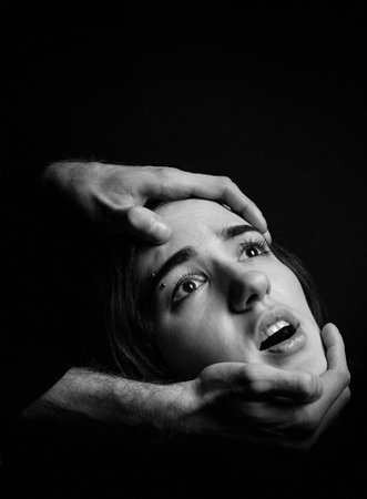 Mens hands hold a womans head on a black background. Fear, suffering. Black and white portrait.
