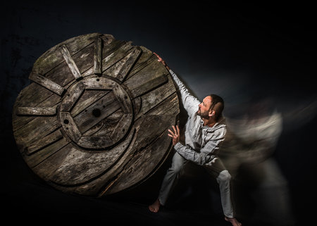 A man tries to stop a wheel rolling towards him. Motion blur.の写真素材