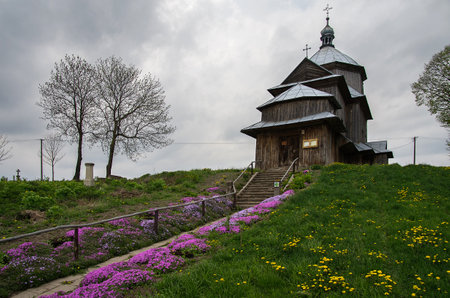 An old wooden Ukrainian Orthodox church with colorful flower beds.の写真素材