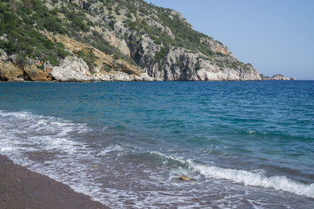 Foamy wave in the blue sea against the backdrop of a mountainous coast.の写真素材