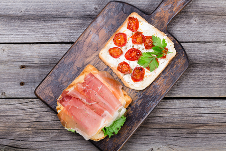 Prosciutto and dried tomato sandwiches on wood desk. Top viewの写真素材