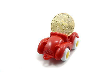 Concept of saving bitcoins for car purchase, Financial success, closeup of red paint plastic toy car carrying bitcoin gold coins isolated on white background.の写真素材