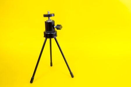 Black mini tripod with steel case and ballhead isolated on yellow background.の写真素材