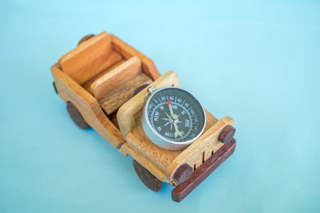 Wooden toy car carrying a compass isolated on sky blue background.