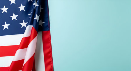 A close-up view of the American flag is draped on the left side of the frame, showing its iconic blue field with white stars and red and white stripes. The flag is partially folded, creating a sense of depth and texture. The right side of the image features a solid, light teal background, offering ample copy space for text or design elements.の写真素材