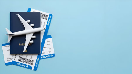 A miniature white airplane rests on top of a dark blue passport. Several airline tickets are fanned out beneath the passport. The items are arranged on a plain, light blue background, suggesting themes of travel and international journeys.の写真素材