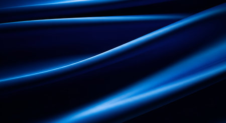 This image features an abstract composition of flowing, deep blue silk fabric. The material is draped in smooth, elegant waves, with highlights and shadows creating a sense of depth and luminosity. The texture appears soft and luxurious, with subtle reflections of light across its surface. The dark background emphasizes the vibrant blue tones and the graceful curves of the fabric.の写真素材