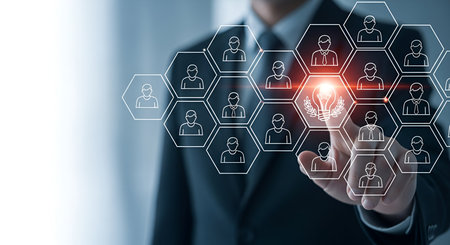 A businessman in a suit is shown with his finger touching a glowing hexagonal icon representing an idea or innovation within a larger network of hexagonal icons depicting people. The network symbolizes connections, teamwork, and human resources. The image conveys concepts of technology, business strategy, and digital interaction.の写真素材