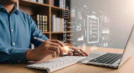 A person's hands are visible as they use a stylus on a keyboard and interact with a glowing digital interface. The interface displays a checklist with completed and pending tasks, along with various data charts and graphs. A laptop is open on a wooden desk, with a bookshelf in the background. The overall scene suggests digital organization and data management.の写真素材
