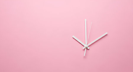 A minimalist clock face is depicted with thin white hour and minute hands pointing to approximately 2:55 on a solid, soft pink background. The clock mechanism is visible at the center where the hands are attached. The composition is clean and uncluttered, with ample negative space to the left of the clock hands.の写真素材