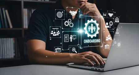 A person's hands are on a laptop keyboard, with a glowing digital interface displaying onboarding process icons. The icons represent various stages of employee integration, including recruitment, training, collaboration, and goal setting. The overall theme is digital business process management and human resources.の写真素材