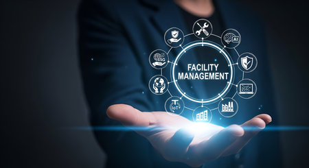 A person in a dark suit holds out their open palm, on which a glowing blue light emanates. Encircling this light is a digital network of white icons representing various aspects of facility management, including tools, AI, ESG, IoT, buildings, and security shields. The central text reads &quot;FACILITY MANAGEMENT.&quot;の写真素材