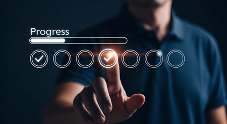 A person's finger is shown touching a digital interface displaying a progress bar and a series of circular icons. Some icons have checkmarks, indicating completion, while others are empty. The word "Progress" is displayed above the progress bar. The image visually represents the concept of tracking progress, task completion, and goal achievement.の写真素材