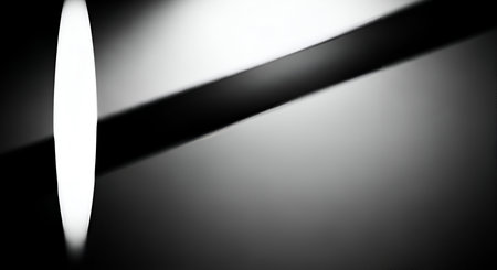 An abstract image featuring a bright white oval light beam on the left side, casting a soft shadow. A dark diagonal band cuts across the frame, creating a strong contrast with the lighter, gradient background. The overall composition is minimalist and focuses on light and shadow play.の写真素材