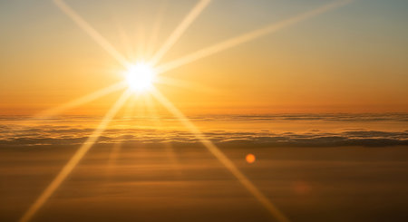 A brilliant sunburst dominates the sky, casting long, bright rays across a layer of fluffy clouds....