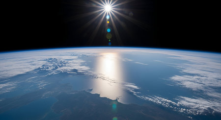 A breathtaking view of Earth from space shows the curvature of the planet with swirling white clouds over the vast blue ocean. The sun shines brightly, creating a brilliant glare and reflection on the water's surface. The blackness of space forms the upper backdrop, highlighting the sun's rays.の写真素材