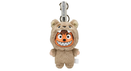 A close-up studio shot features a fluffy plush toy keychain dressed in a brown bear costume. The...