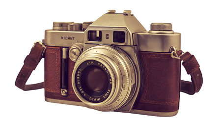 An antique film camera is shown with its brown leather case and strap. The camera has a silver metal body with a prominent lens assembly featuring an aperture ring. Various dials, knobs, and buttons are visible on the camera's body and top. The leather case has a textured finish.の写真素材